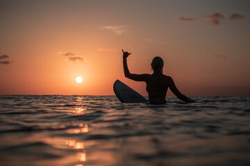 Portrait from the water of surfer girl with beautiful body on surfboard in the ocean at colourful sunset time