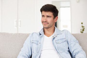 Portrait young serious man sitting on couch home.