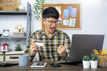 Asian man holding credit card to Online shopping with laptop computer and entering security code 
