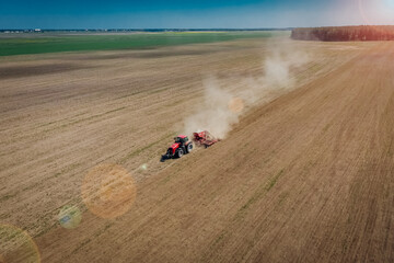 A tractor with a plow plows agricultural fields for sowing wheat. Aerial view