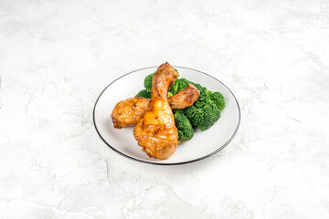 Fried chicken legs with broccoli on a white plate