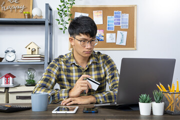 Asian man holding credit card to Online shopping with laptop computer and entering security code
