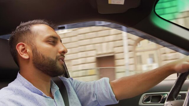 Side View Of Young Middle Eastern Man Nodding Head To Music While Driving Car Down City Road