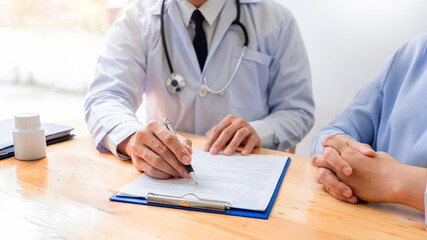 Fototapeta premium Charming Asian male doctor giving advice and medical informations and diagnosis to a female patient at consulting room in clinic.