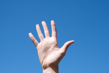 Gesture closeup of a woman's hand showing five fingers, isolated against a blue sky, sign language symbol number five