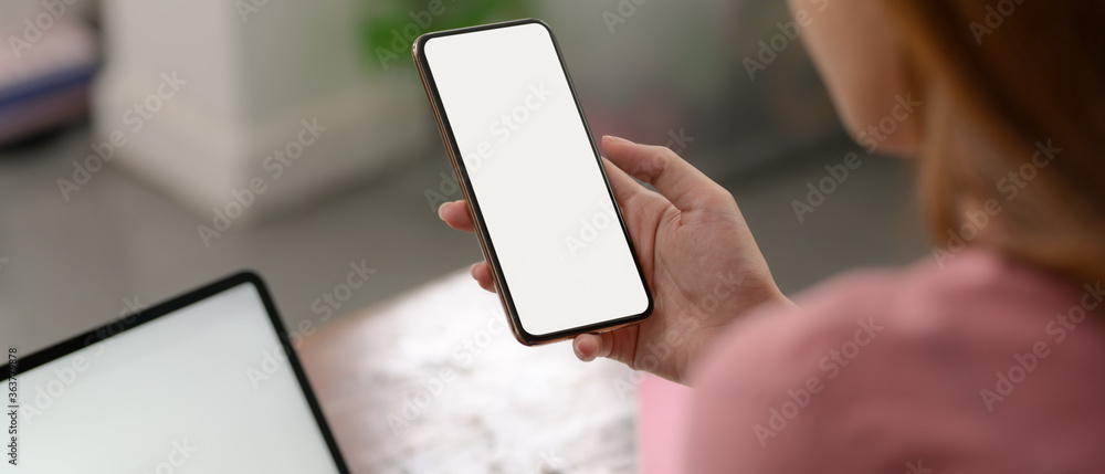 Poster a woman using mock-up smartphone to relax while working with mock-up laptop on wooden table