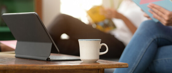 Digital tablet with keyboard and coffee cup on wooden coffee table in living room