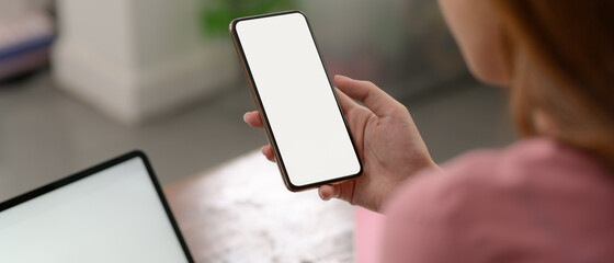 A woman using mock-up smartphone to relax while working with mock-up laptop on wooden table