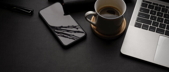 Dark modern workspace with laptop, smartphone, coffee cup, office supplies and copy space