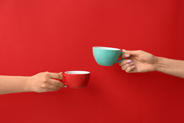 Hands with cups of hot coffee on color background