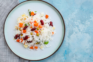Plate with tasty rice, beans and vegetables on color background