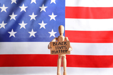 Mannequin with text BLACK LIVES MATTER on poster near flag of USA