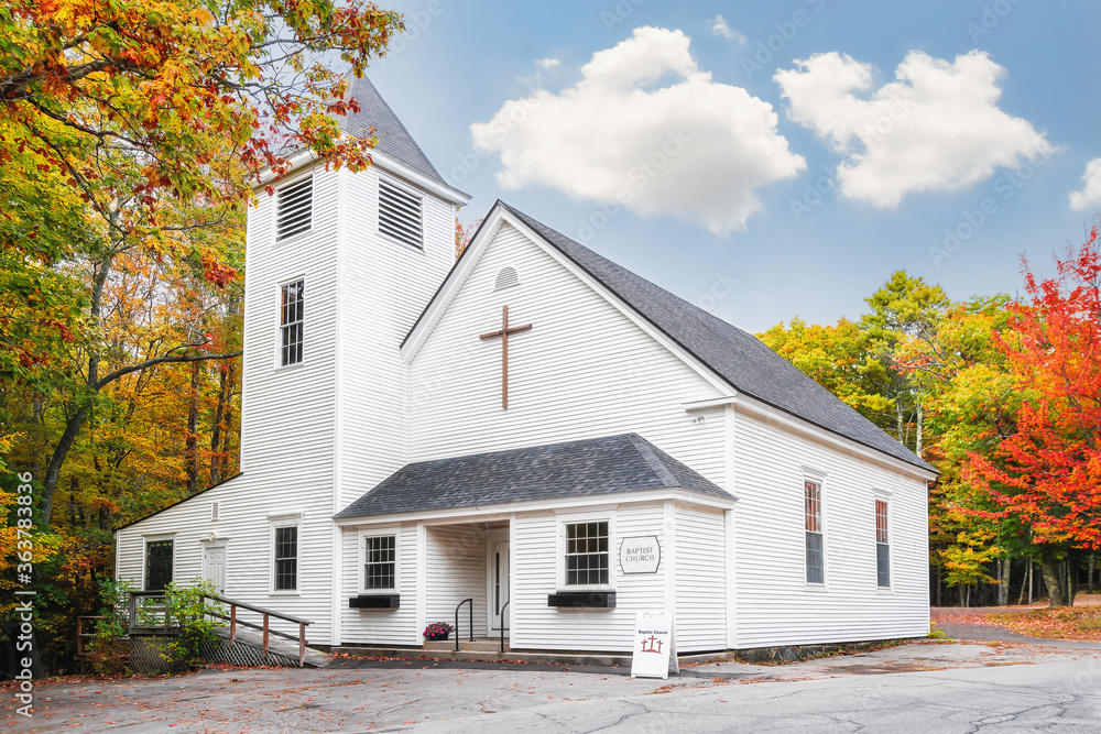 Wall mural White country Baptist church surrounded by beautiful foliage colors in New England autumn. White clouds and blue sky background.