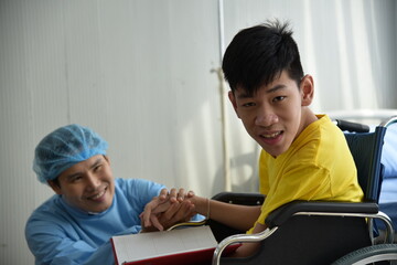 An Asian male Doctor taking care and look after Disabled boy Patient /cripple who can not help himself sitting on wheelchair in hospital/Disability