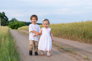 The little boy is carefully holding the little girl's hand they are looking into the distance