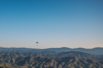山脈の上を飛ぶパラグライダーを空撮