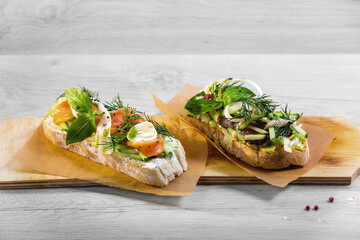 Bruschetta, grilled ciabatta with salmon and veal are on a light wooden background.