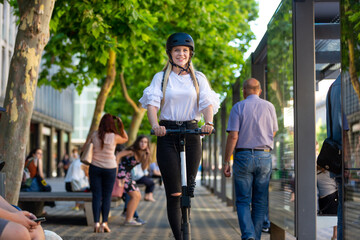 Trendy fashinable teenager, beautiful blonde girl riding public rental electric scooter in urban...