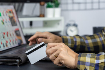Asian man holding credit card to Online shopping with laptop computer and entering security code
