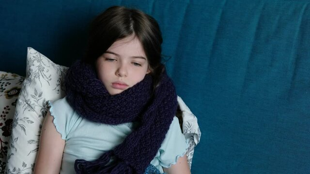 little girl is sick, lies on a sofa in a warm scarf, coughs