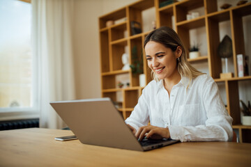 Smiling young woman using laptop at home, portrait.