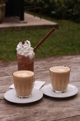two cups of coffee and one cup of chocolate milkshakes on a wooden table.