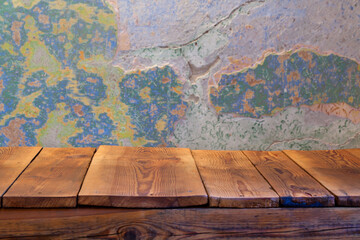 Pusty blat drewnianego stołu zbitego ze starych desek, w tle obdrapana wielokolorowa ściana, pomalowana farbą kredową. - obrazy, fototapety, plakaty