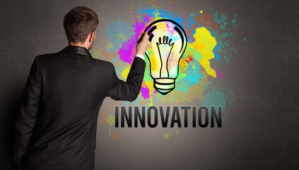 businessman drawing colorful light bulb with INNOVATION inscription on textured concrete wall, new business idea concept