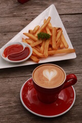 a cup of coffee and french fries on a wooden table.