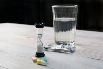 Hourglass, pills and glass of water on wooden table. limited lifetime.