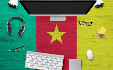 Cameroon flag background with headphone,computer keyboard and mouse on national office desk table.Top view with copy space.Flat Lay.