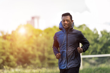 Obraz premium A man in sport hoodie jogging in the city park in the evening after stressful work. Runner jogging training and workout exercising power walking outdoors in forest city. Stock photo