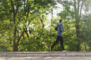 A man in sport hoodie jogging in the city park in the evening after stressful work. Runner jogging training and workout exercising power walking outdoors in forest city. Stock photo