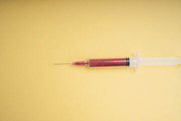 Glitter blood in syringe over yellow background.