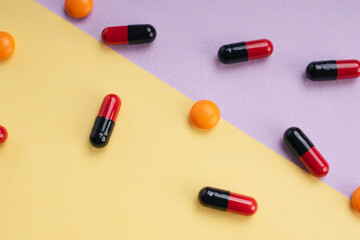 Red and black medicine pill capsule and orange circle pill over pastel background.