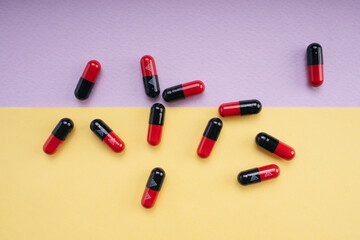 Top view - Black and red medicine pill capsule over pastel background.