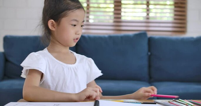Cheerful asian cute small kid girl artist playing alone drawing coloring picture with pencils, focused smart preschool child enjoying creative art hobby activity at home, children development concept.
