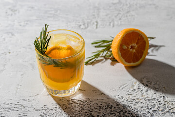 Refreshment drink with orange  and rosemary herb on white concrete background. Summertime beverage...