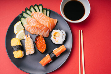 Japanese sushi and maki rolls with salmon sashimi on black plate with soy sauce and chopstick.