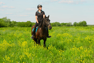 One Caucasian horsewoman is standing in the field on the sunny hot day.