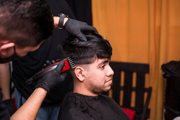 Young hairdresser's hands making haircut to man at barbershop
