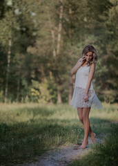 girl in a white dress walks through the woods