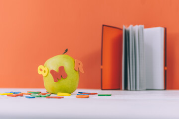 Concept Back to School. Green apple with colored letters and notepad background.