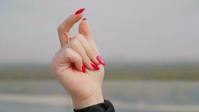 Close up woman hand with red nail polish snaps fingers outdoors. 4K slow motion footage