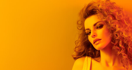 High Fashion. Woman in colorful neon gold light, make-up. Sexy blond girl, stylish curly hair, trendy makeup. Golden neon portrait. Creative beauty, fashionable model face, voluminous hairstyle