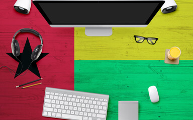 Guinea flag background with headphone,computer keyboard and mouse on national office desk table.Top view with copy space.Flat Lay.