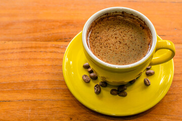 yellow cup coffee on wood background and coffee bean on the yellow plate or wooden table