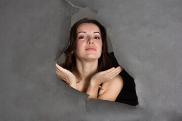 a young woman looks out through a hole in the gray paper background.