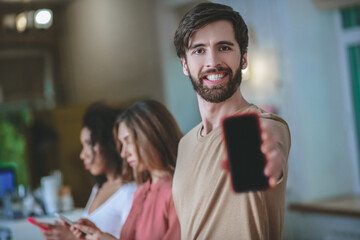 Smiling man holding smartphone in outstretched arm, two girls behind