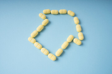 Yellow medicine pills in shape of arrow and house over blue background.